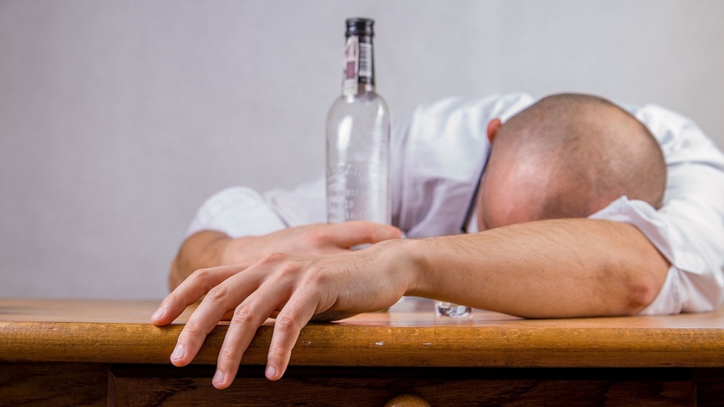 Man slumped over a table with an alcohol bottle in his hand