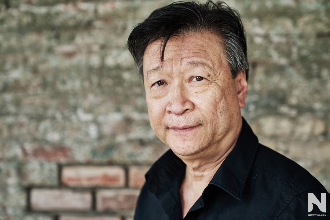 Close-up portrait of Tzi Ma beside a brick wall